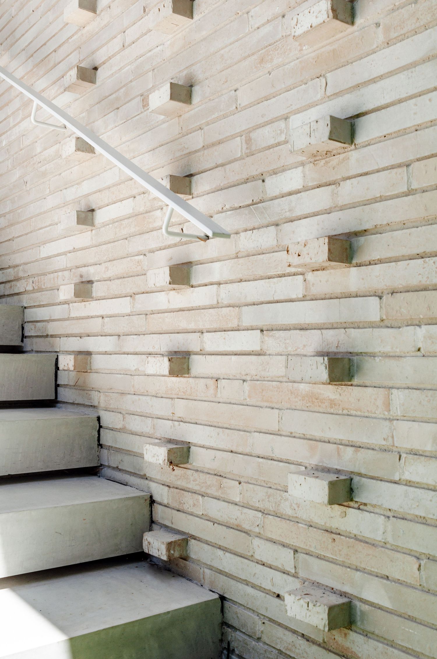 Minimalist staircase with white concrete steps and geometric wall pattern featuring recessed squares.