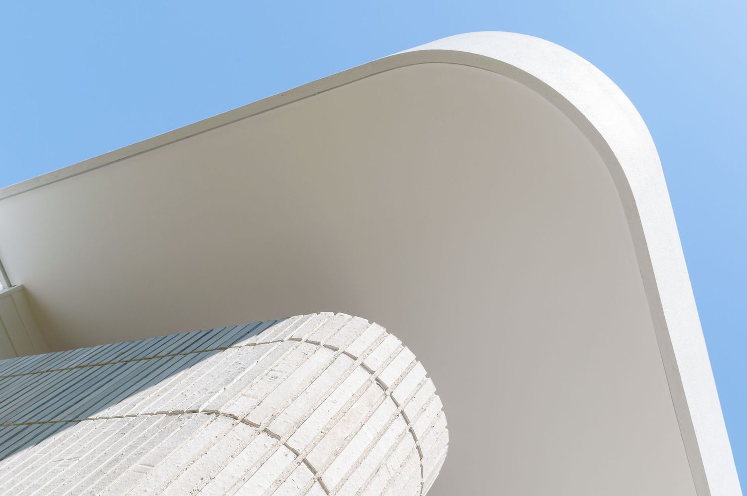 Architectural detail of curved white overhang against bright blue sky.