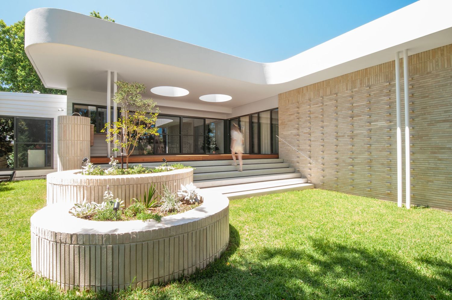 Contemporary house entrance featuring curved concrete planters and wide steps against textured stone wall.