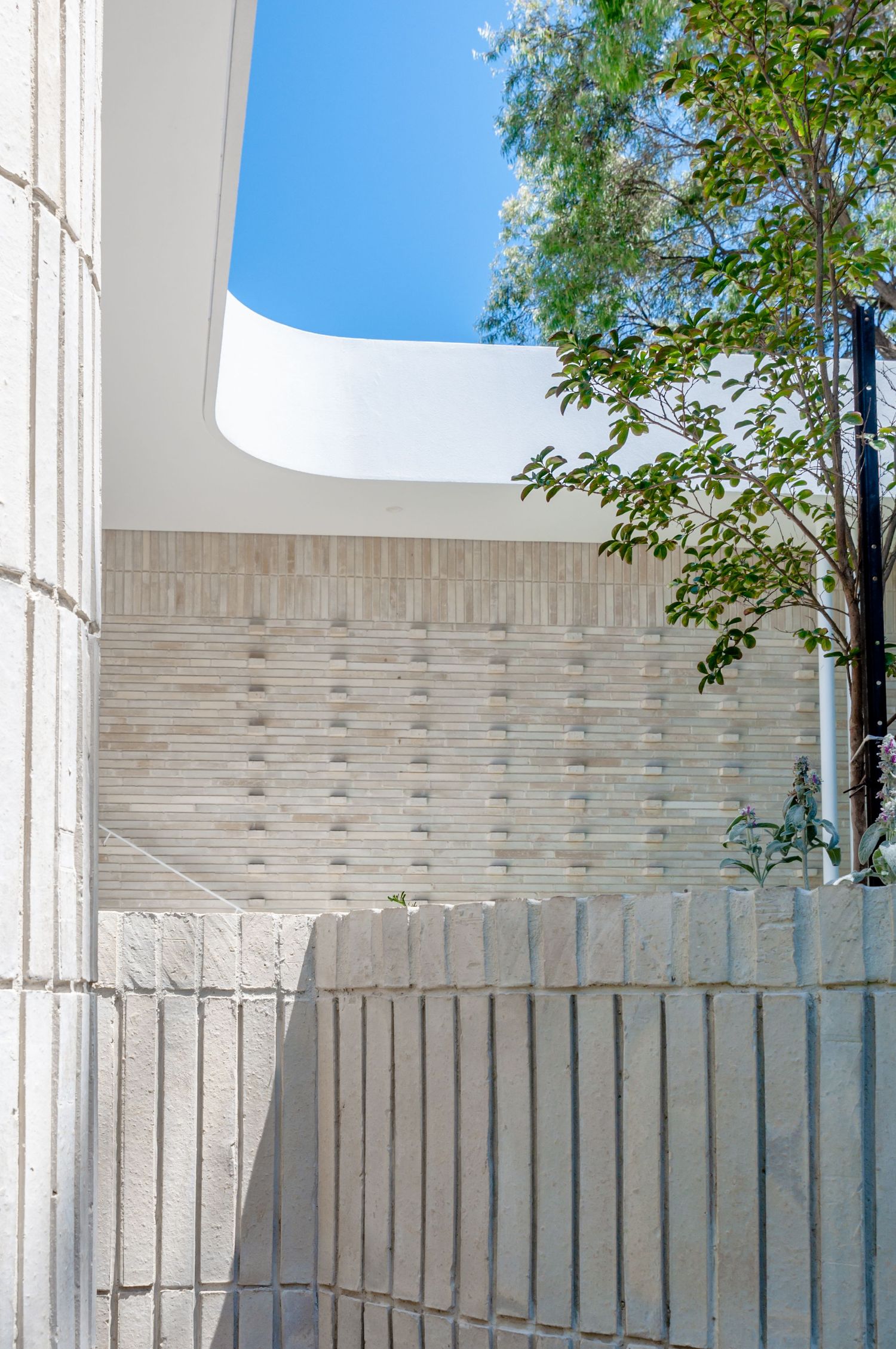 Outdoor courtyard with textured concrete walls and curved opening revealing blue sky above.