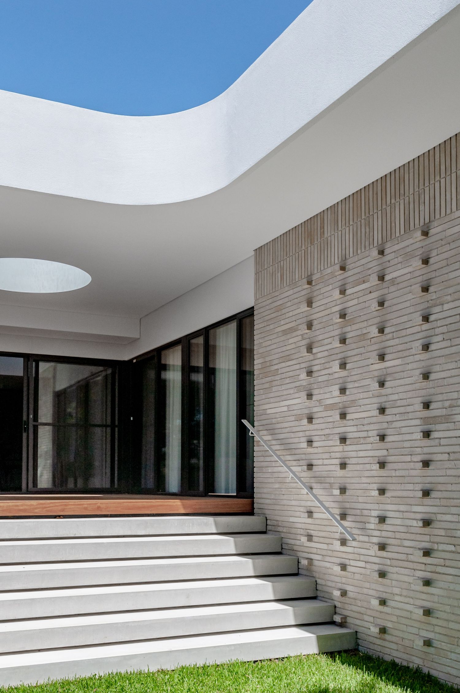Contemporary house entrance with curved white roof, concrete steps, and textured wall.