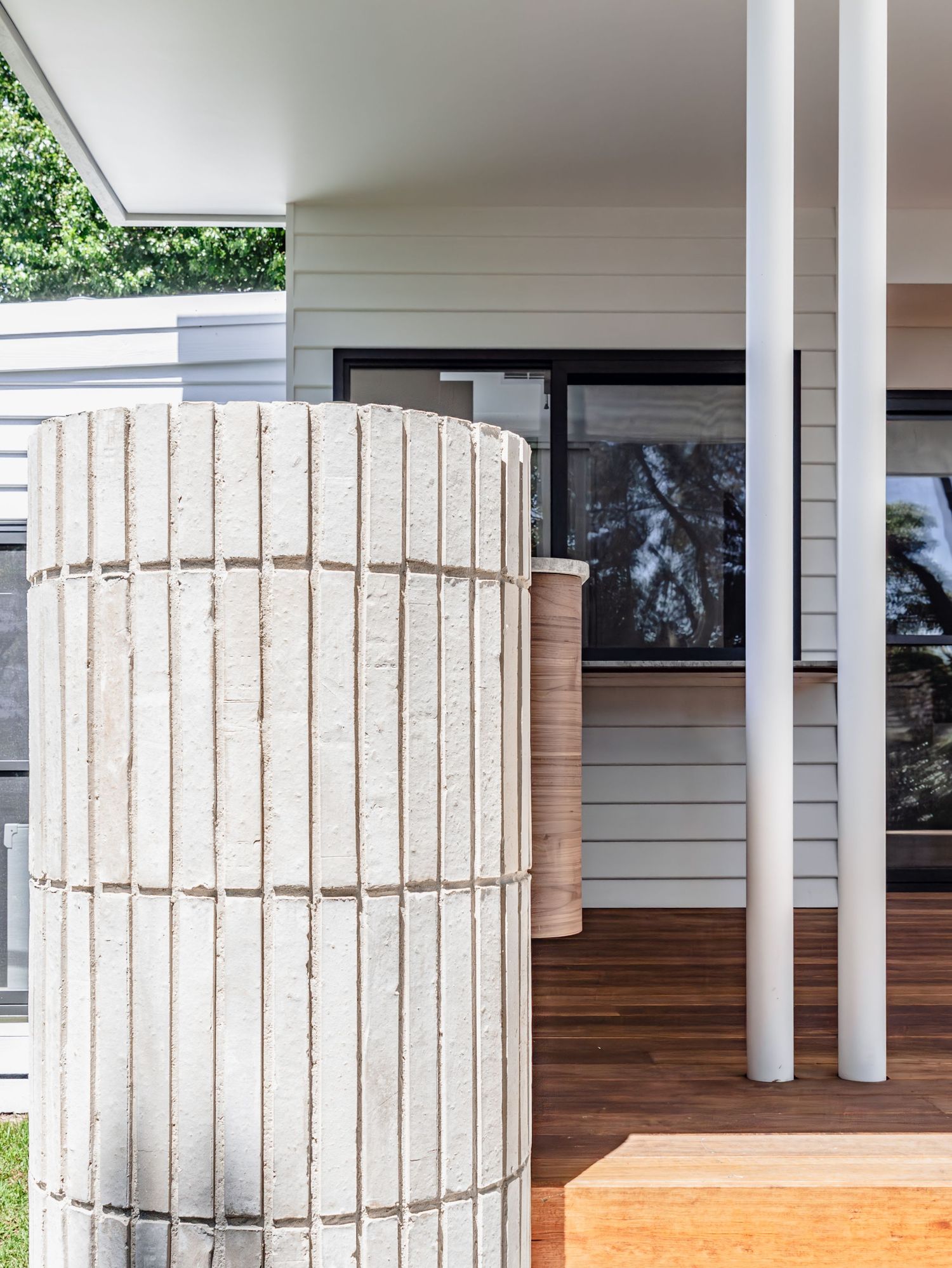 Cylindrical concrete column detail with wooden deck and white exterior siding.