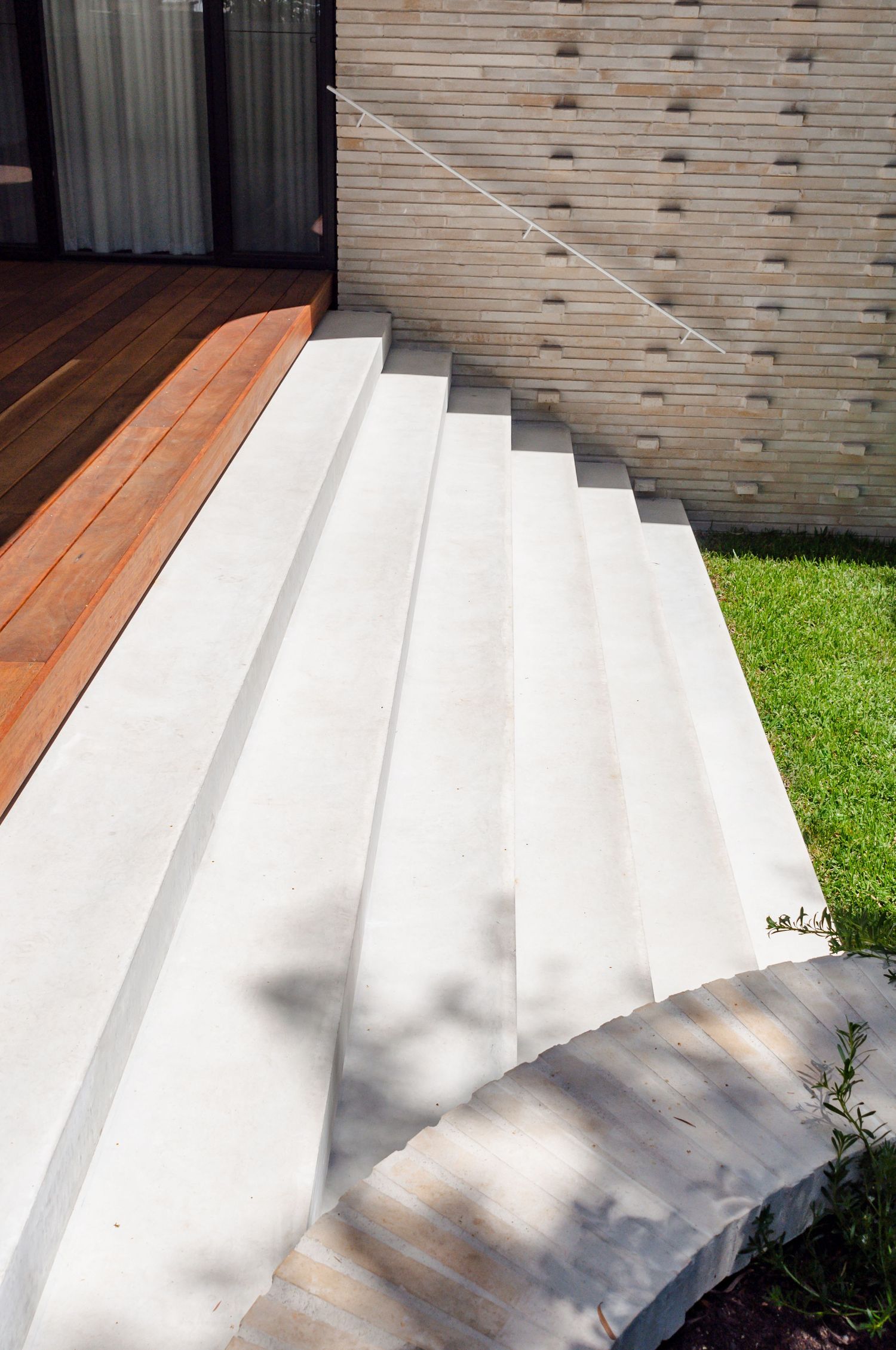 White concrete steps leading to wooden deck with textured wall and landscaping.