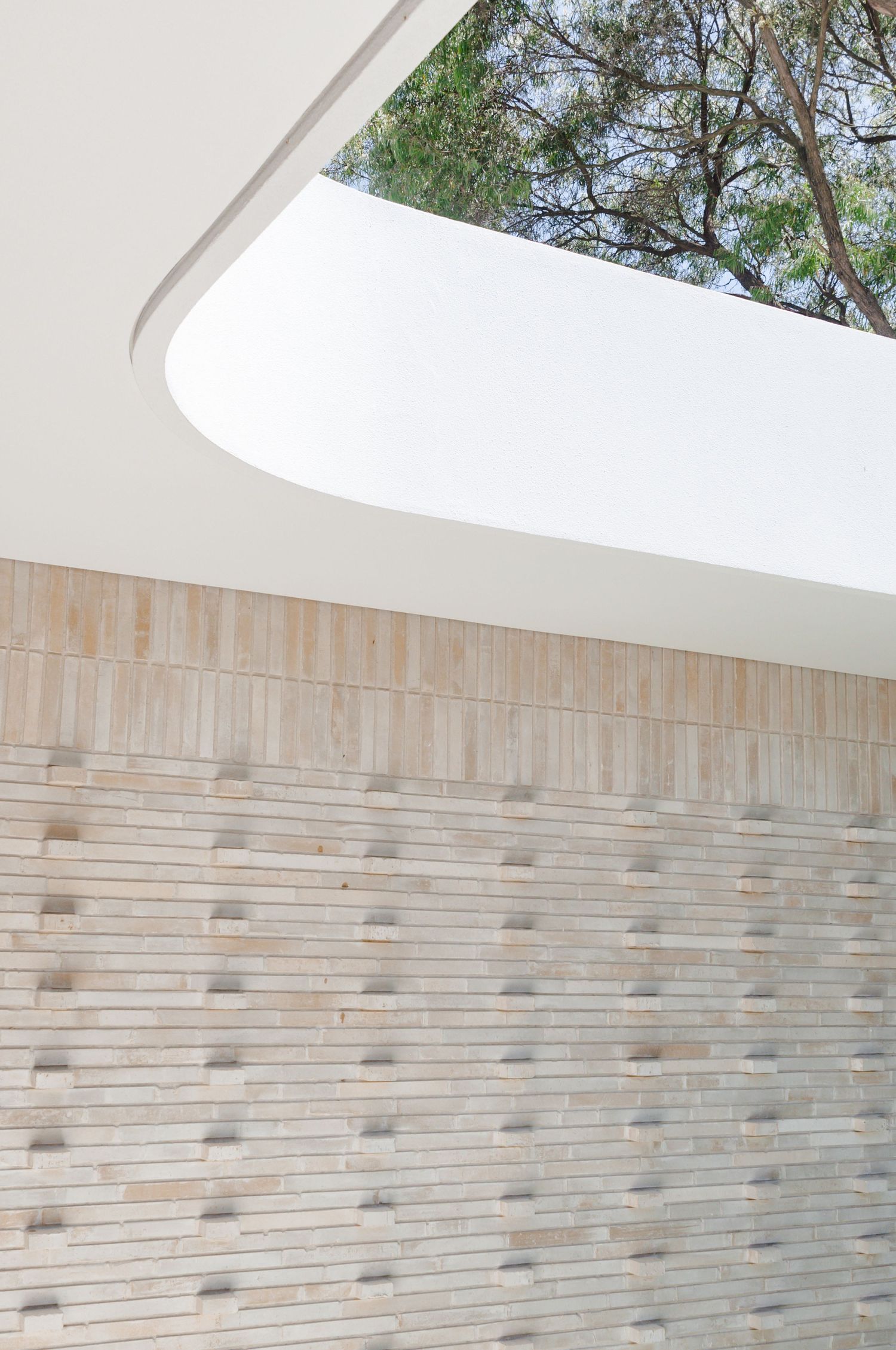 Curved white architectural detail with textured stone wall and tree canopy above.