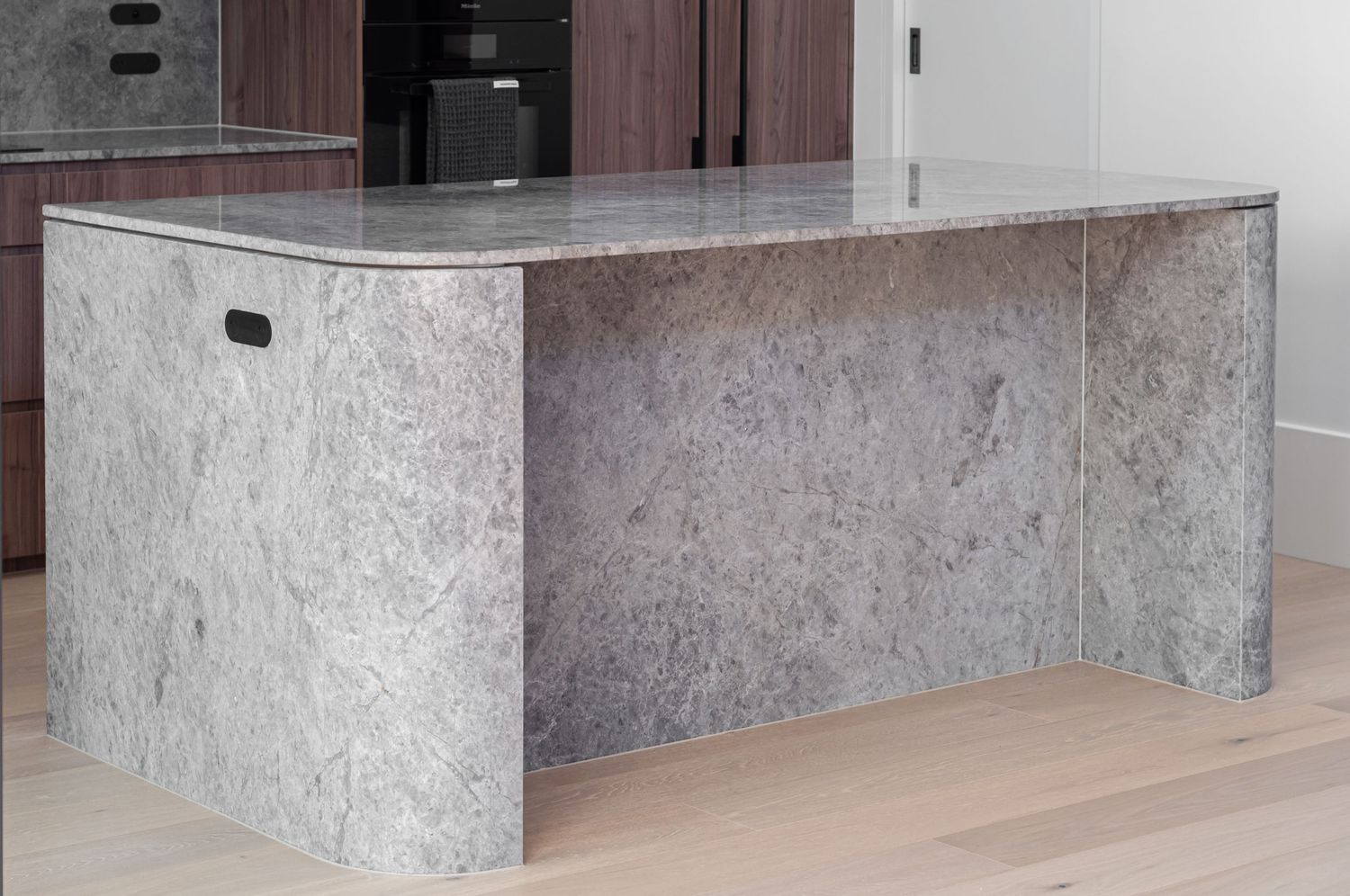 Contemporary kitchen island with textured stone finish and light wooden flooring.