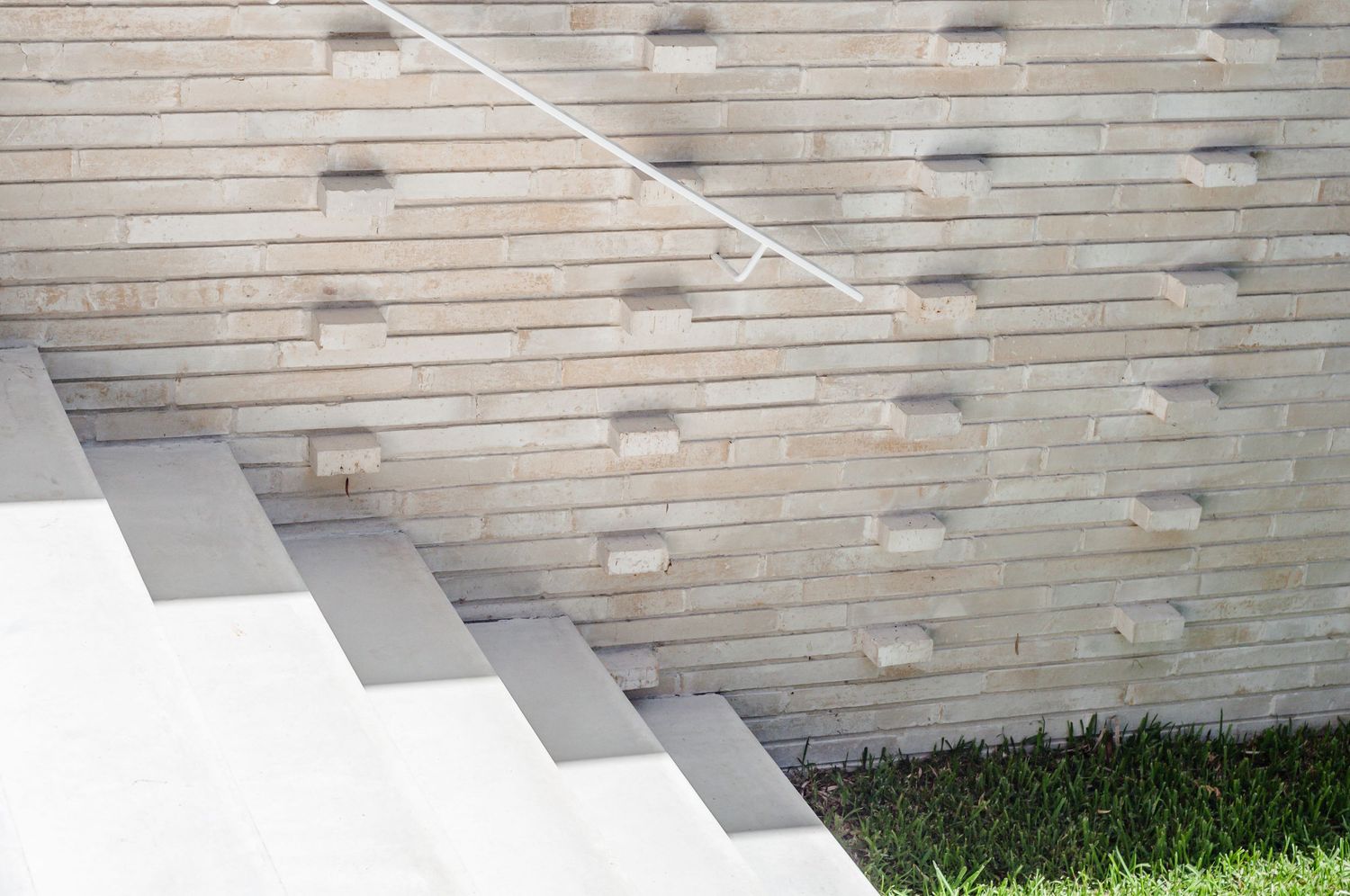 Minimalist white steps against a textured brick wall with protruding brick details.