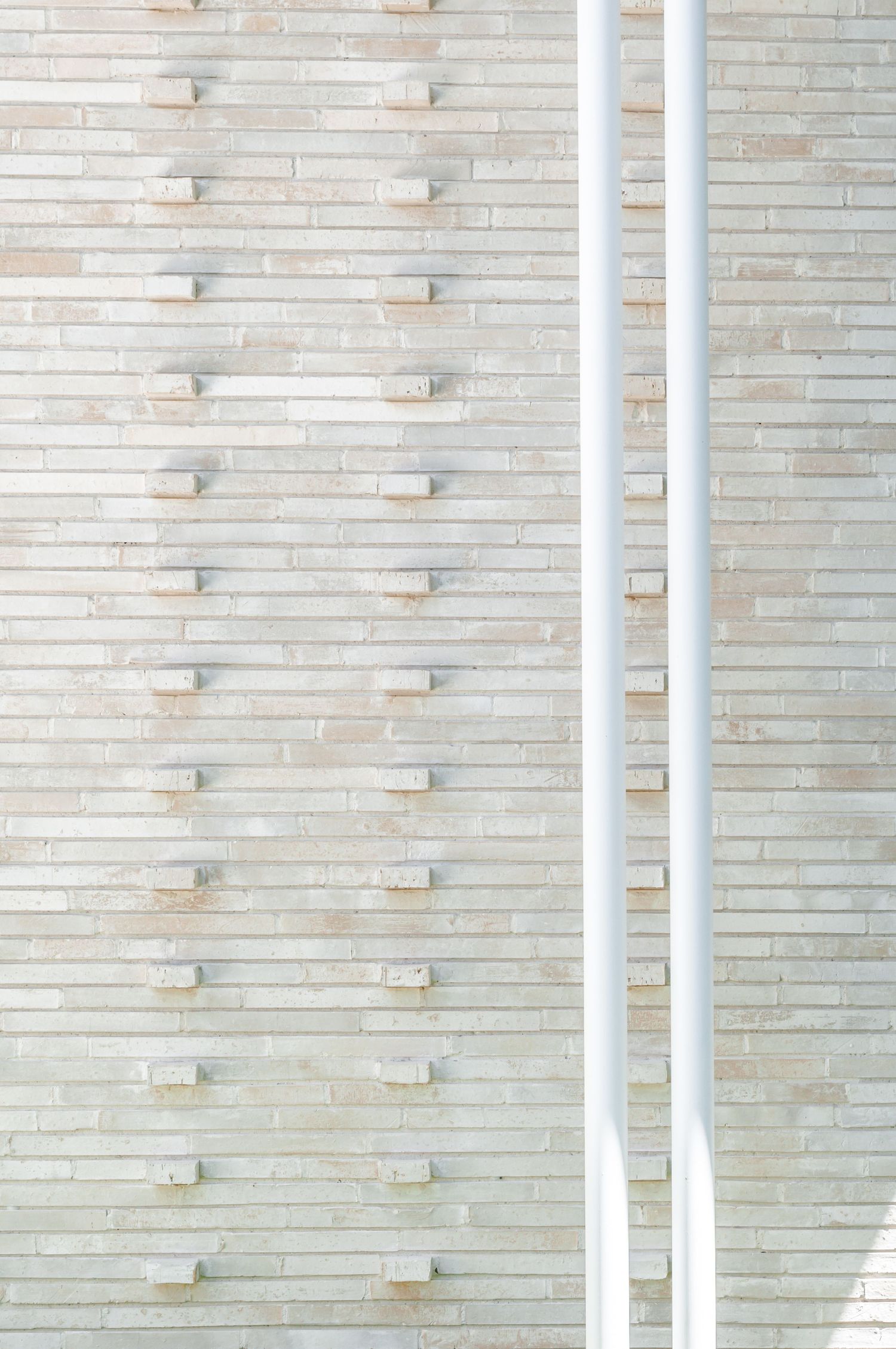 Vertical white downpipe against textured brick wall with geometric pattern.