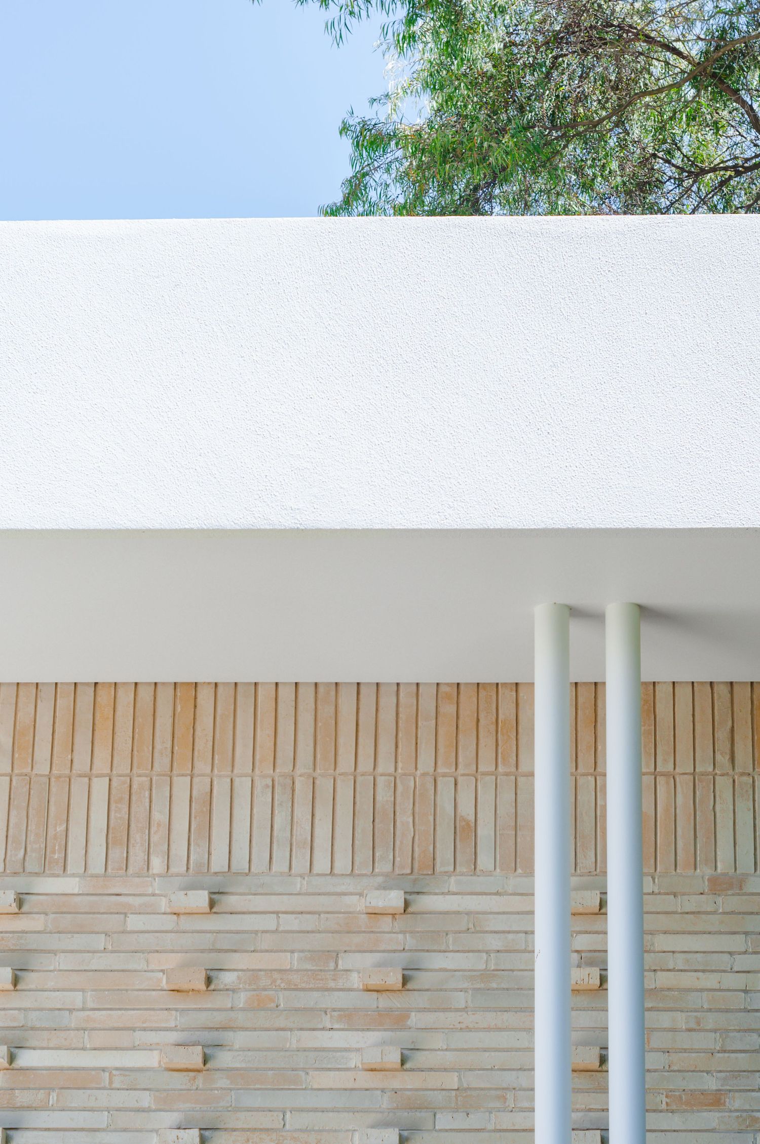 Modern exterior featuring white columns against textured brick wall under clean white overhang.