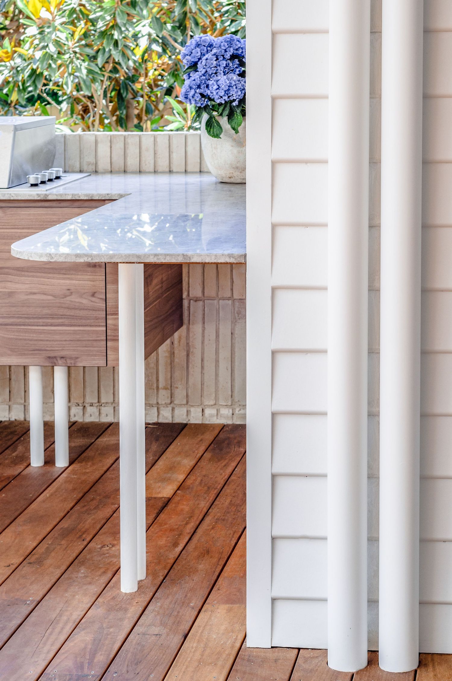 Modern outdoor kitchen counter with white marble top and blue hydrangea flowers on wooden deck.