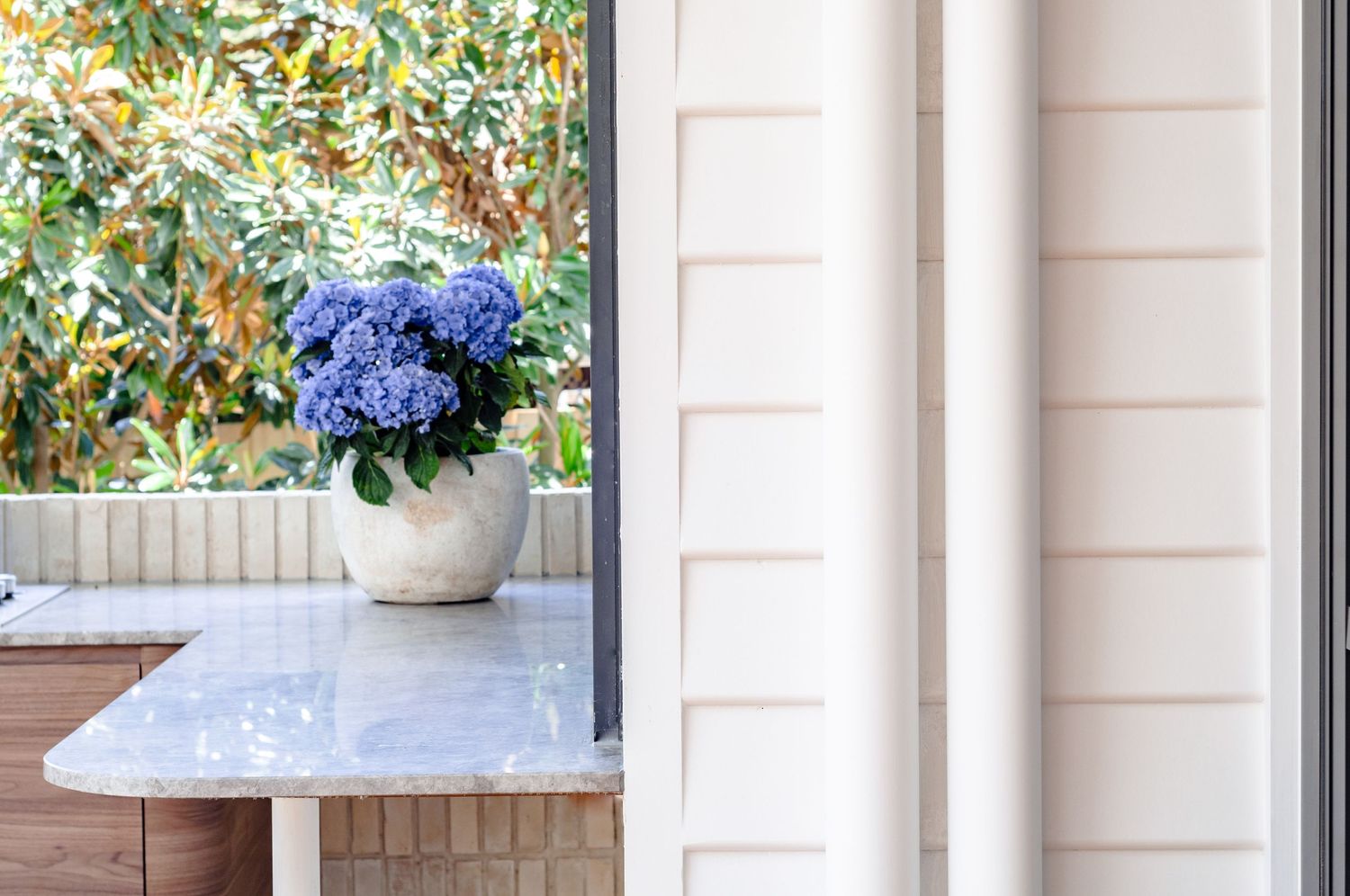 White column framing a marble countertop with blue hydrangeas in a ceramic pot.
