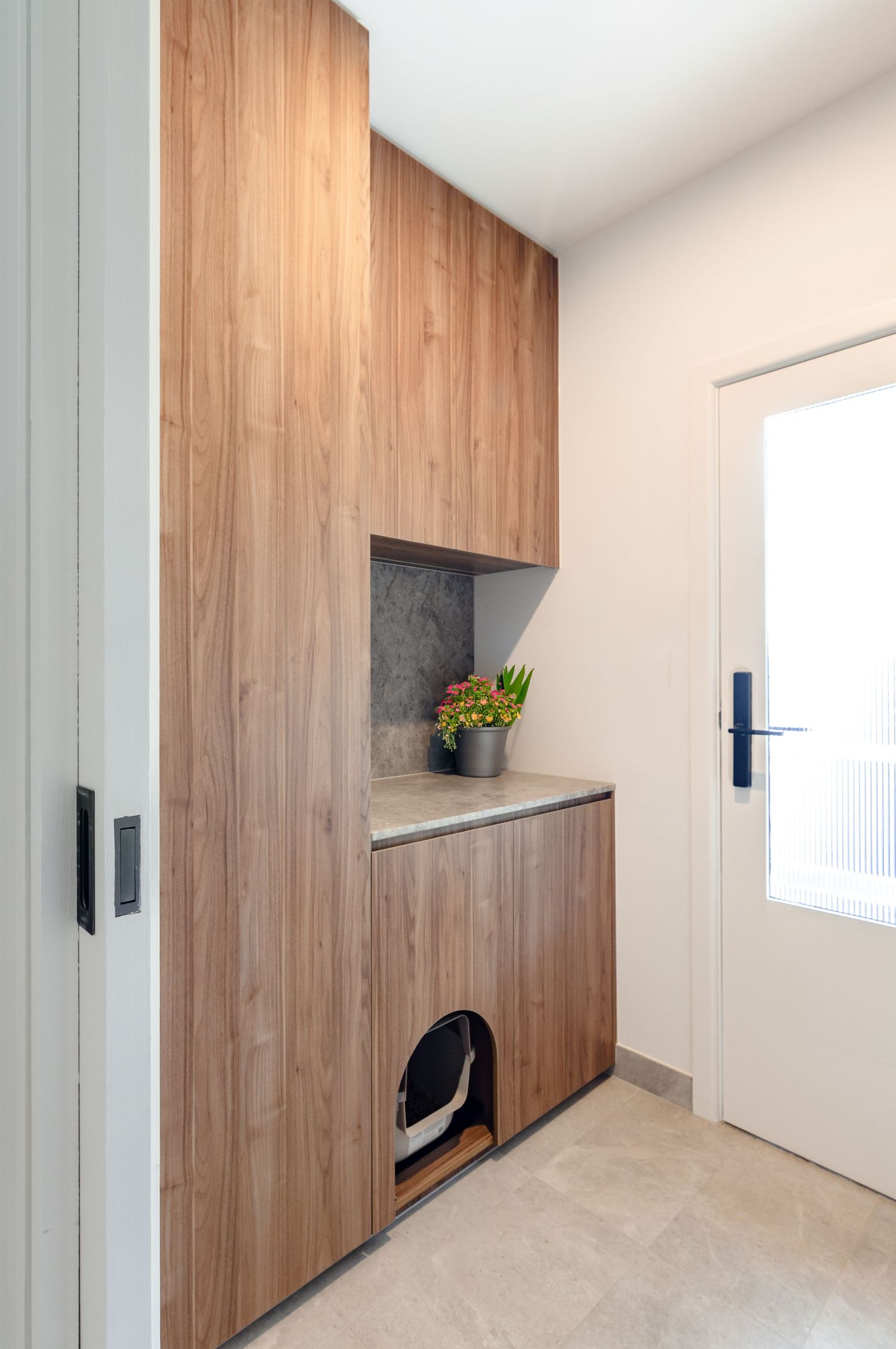 Modern wooden cabinet with built-in storage nook and grey stone countertop in minimalist entryway.