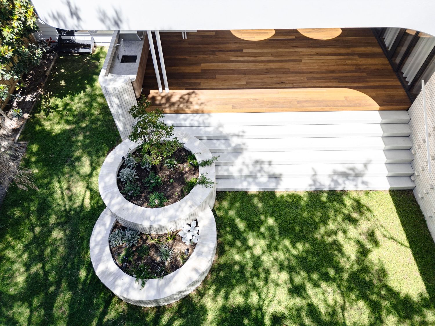 Aerial view of curved white planters and wooden deck in modern backyard design.