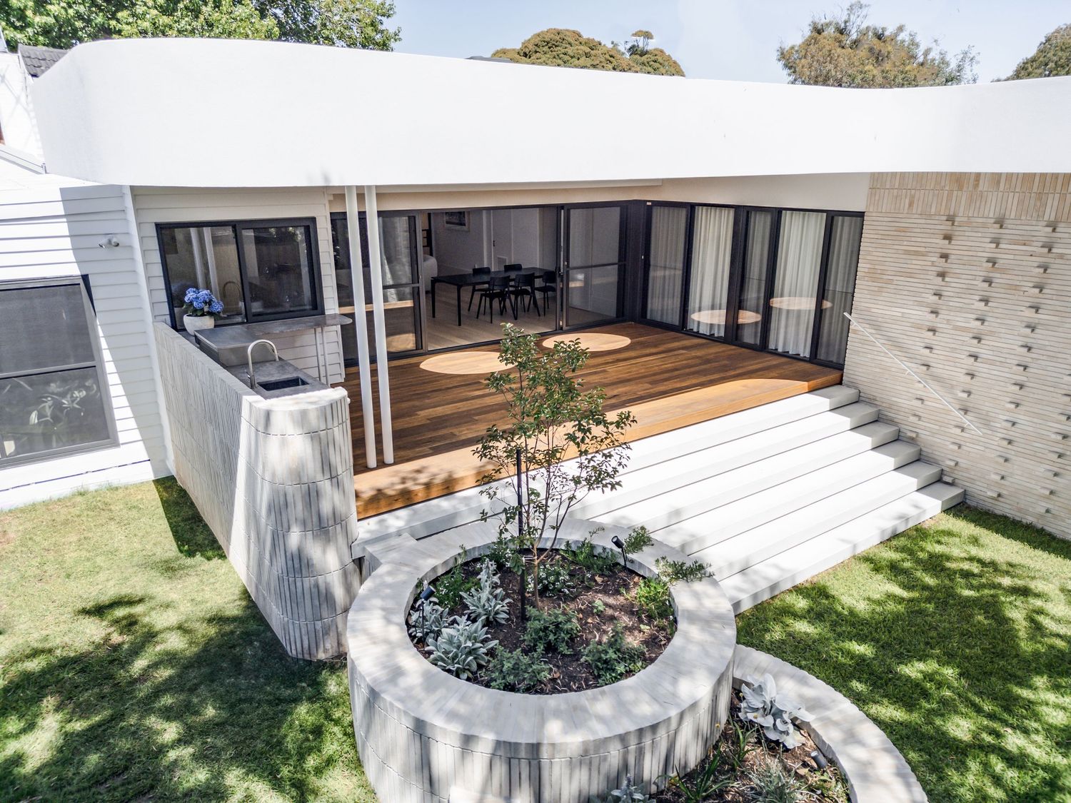 Modern white house with deck and curved garden planters viewed from above.