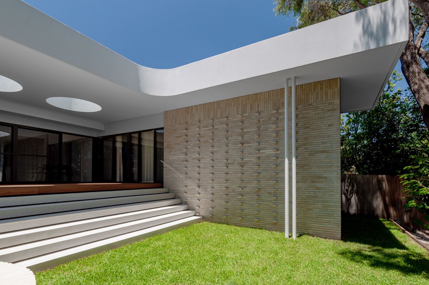 Modern residential exterior featuring white overhang with circular skylights and textured wall detail.