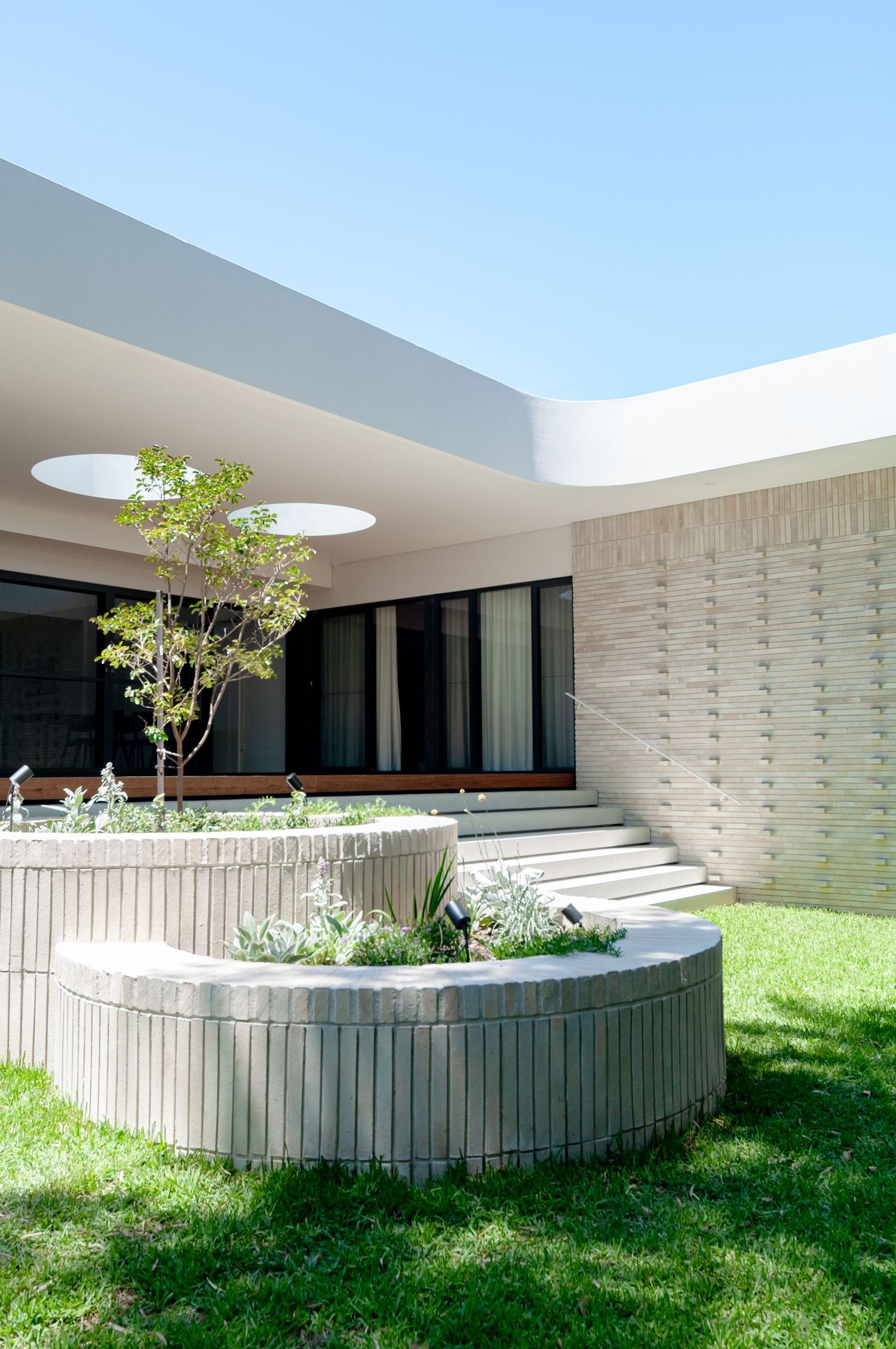 Architectural detail of modern home entrance with circular planters and natural light from ceiling skylights.