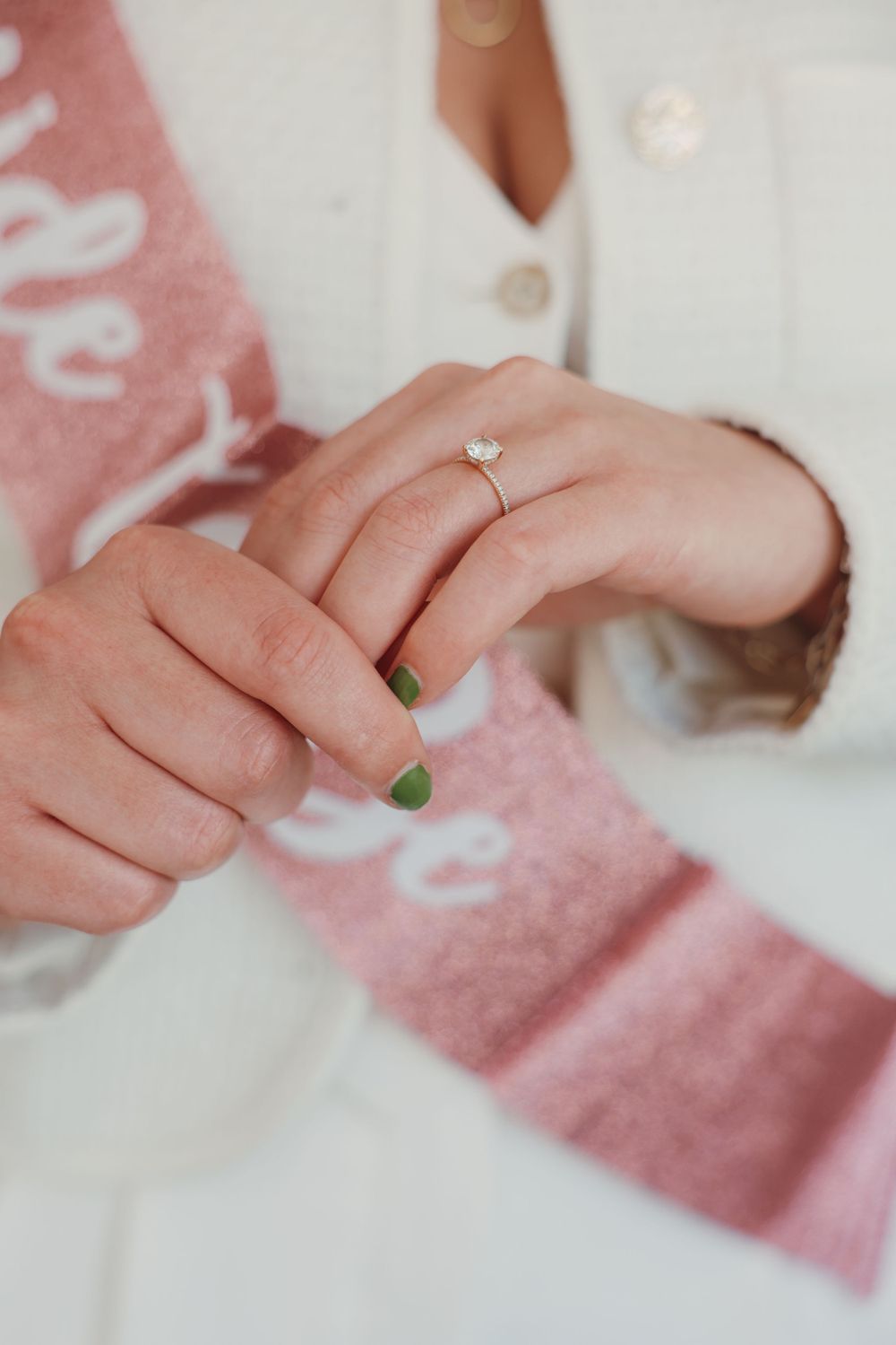 Close-up of engagement ring with pink sash in background.