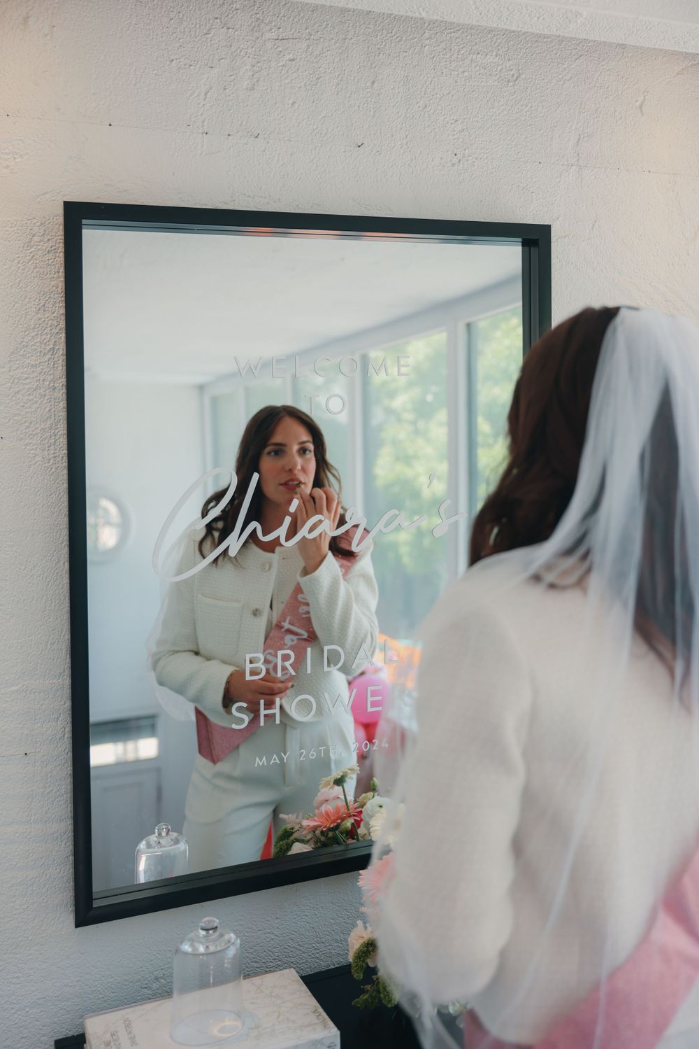 Woman in white looking at her reflection in a bridal shower welcome mirror.