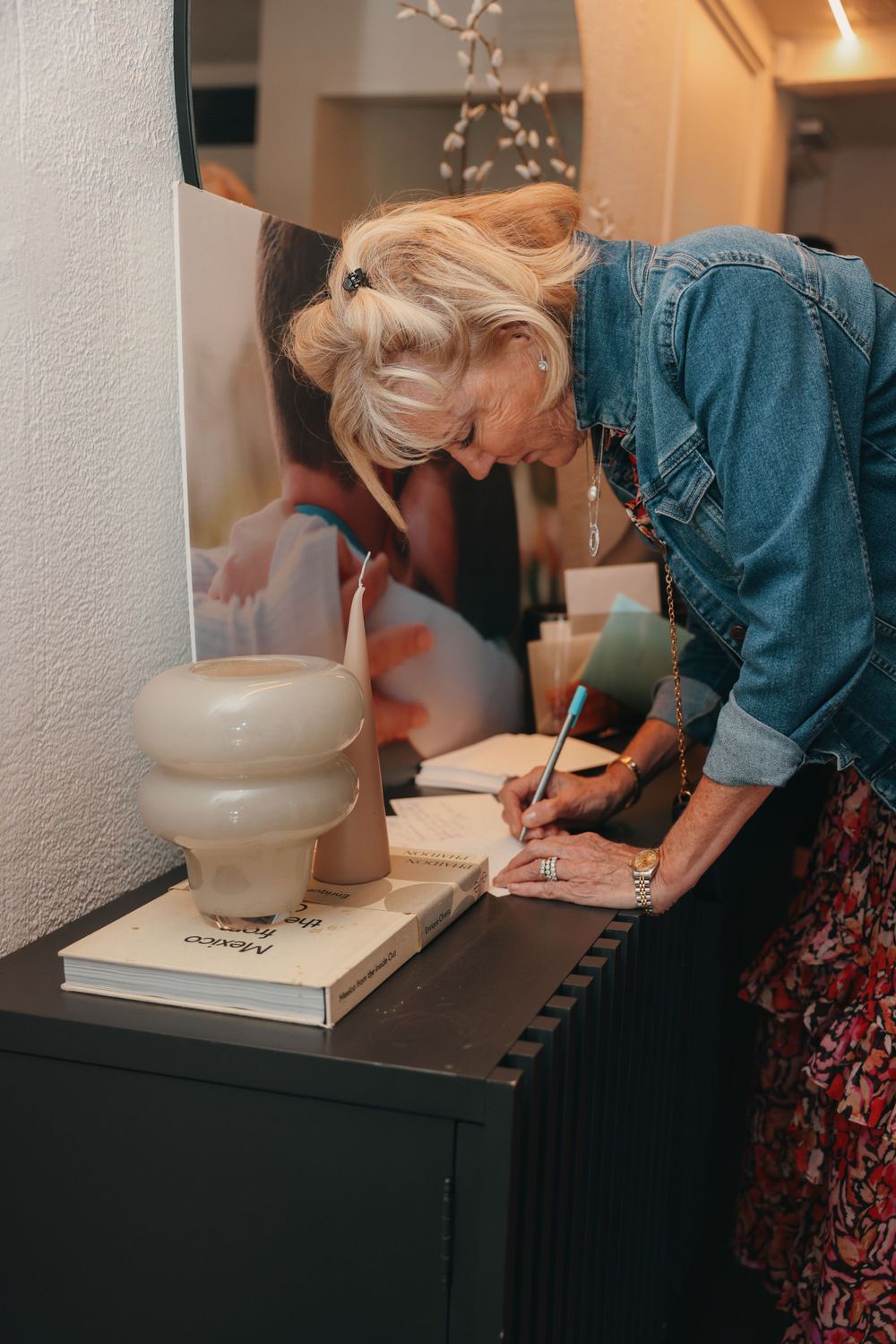 Person writing at a black desk with decorative lamp and mirror.
