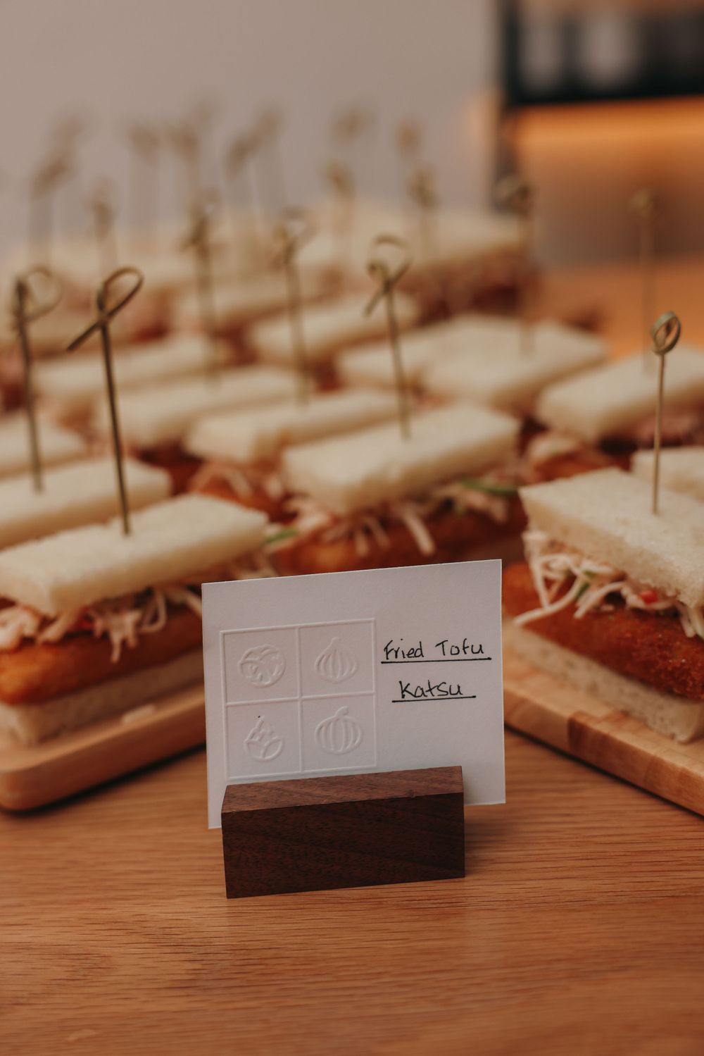 Small sandwich appetizers with toothpicks arranged on a wooden board with a menu card display.