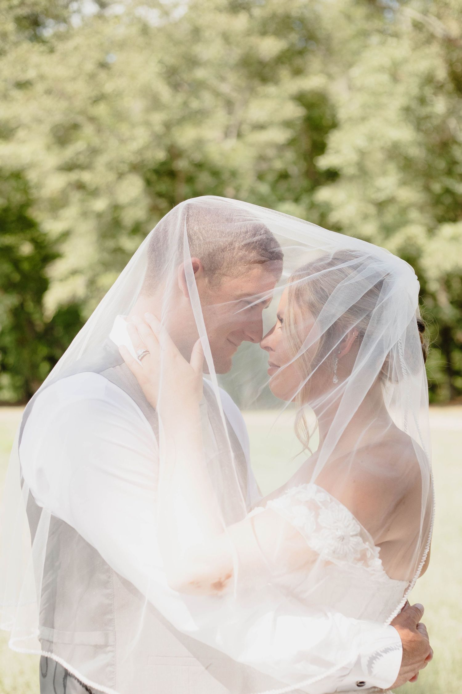 Newlywed couple sharing intimate moment under wedding veil outdoors.