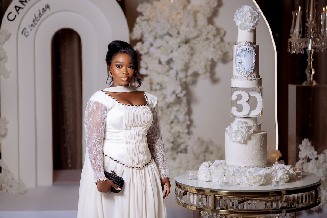 Elegant wedding scene with figure in white lace dress standing next to ornate tiered cake.