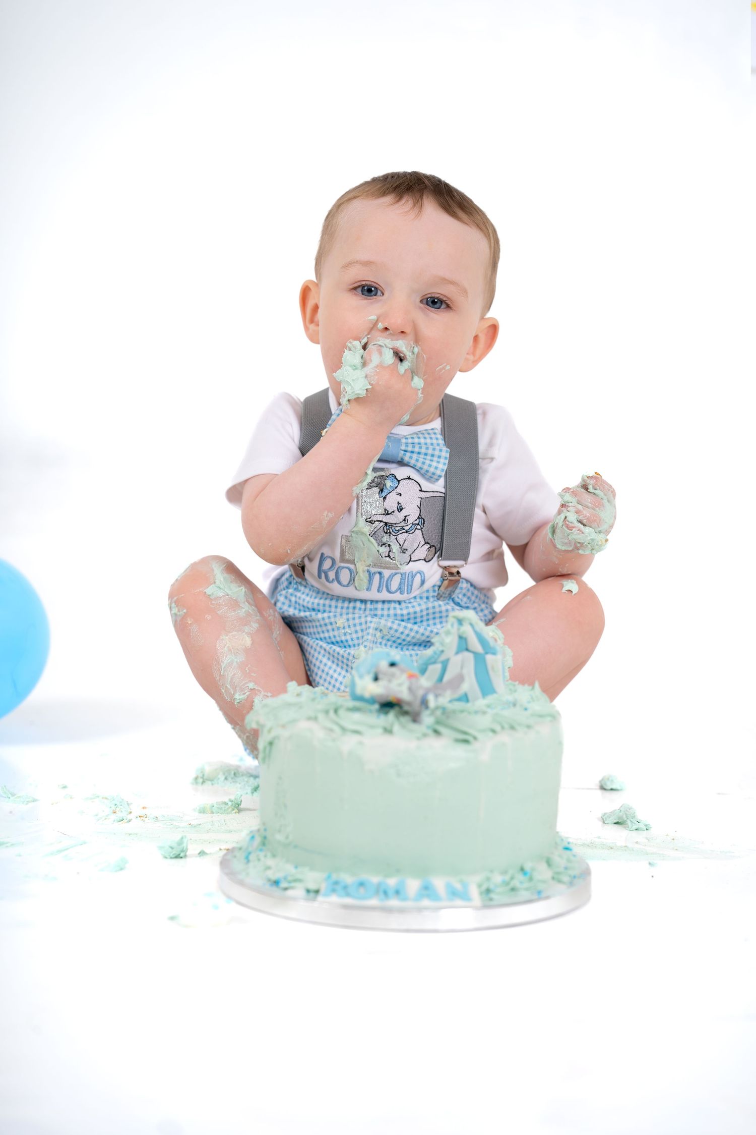 Baby in grey outfit enjoying messy first birthday cake smash with light blue frosting.