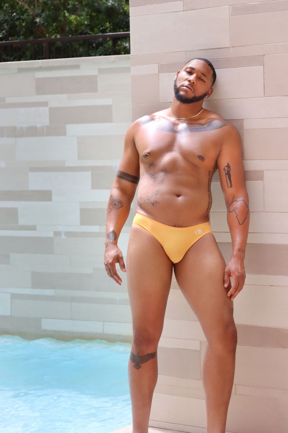 Athletic person in yellow swimwear poses against light colored wall near swimming pool.