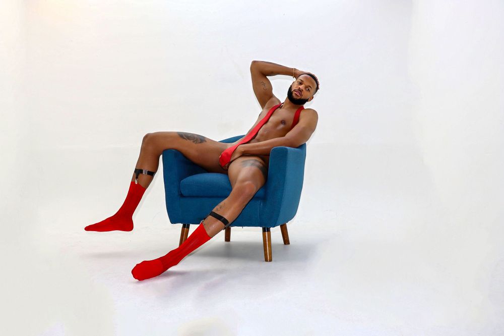 A person in red boots lounges dramatically across a retro blue armchair against a white backdrop.
