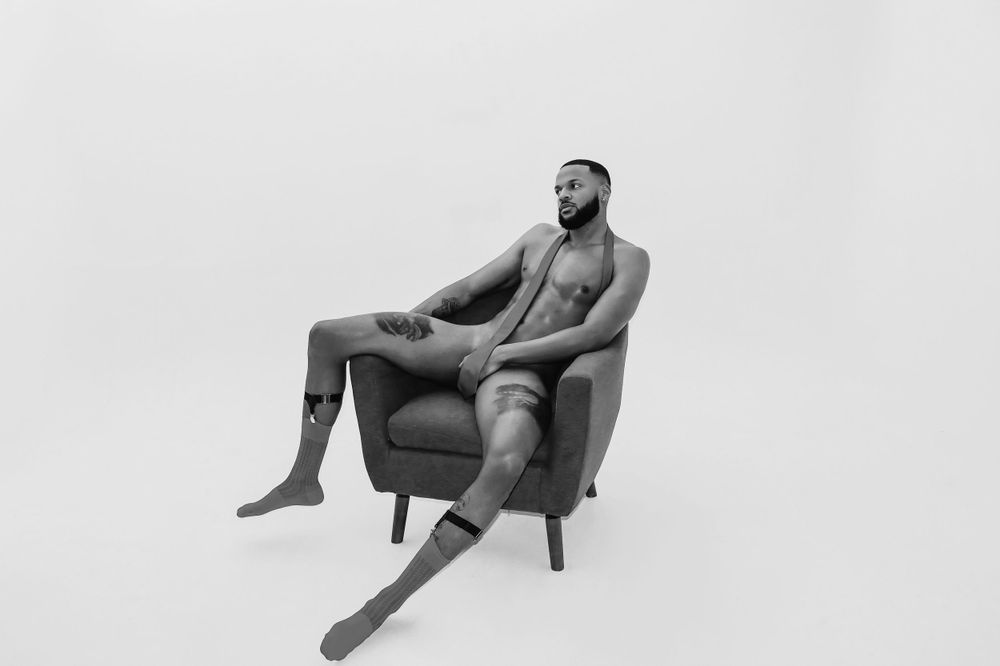 Black and white artistic portrait of a person reclining in a modern armchair against a white backdrop.