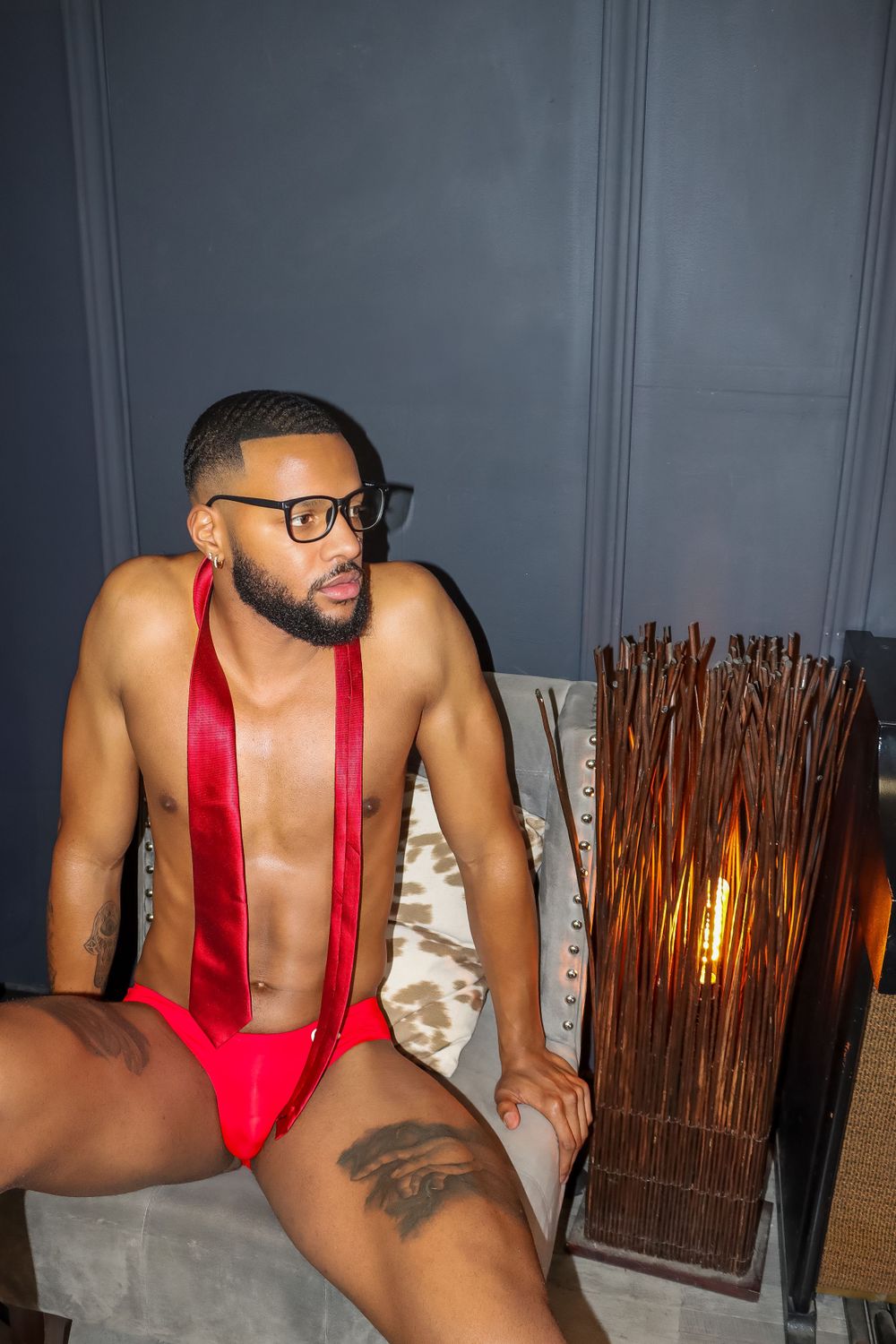 Artistic portrait featuring red suspenders and glasses with a decorative wooden lamp in background.