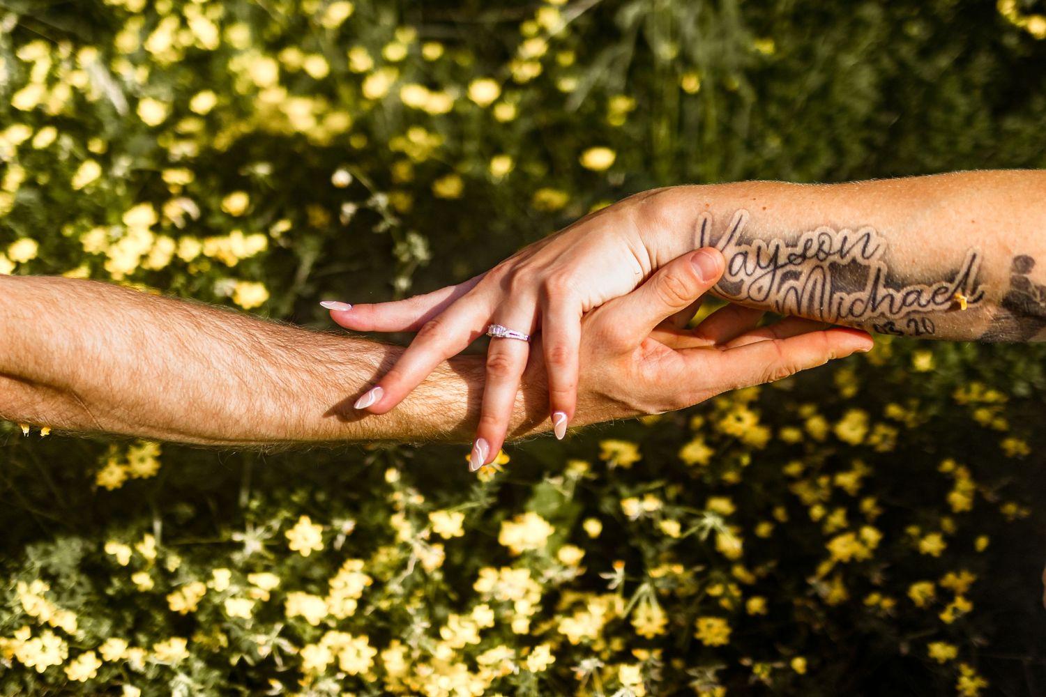 Two hands reaching toward each other against a background of yellow flowers.
