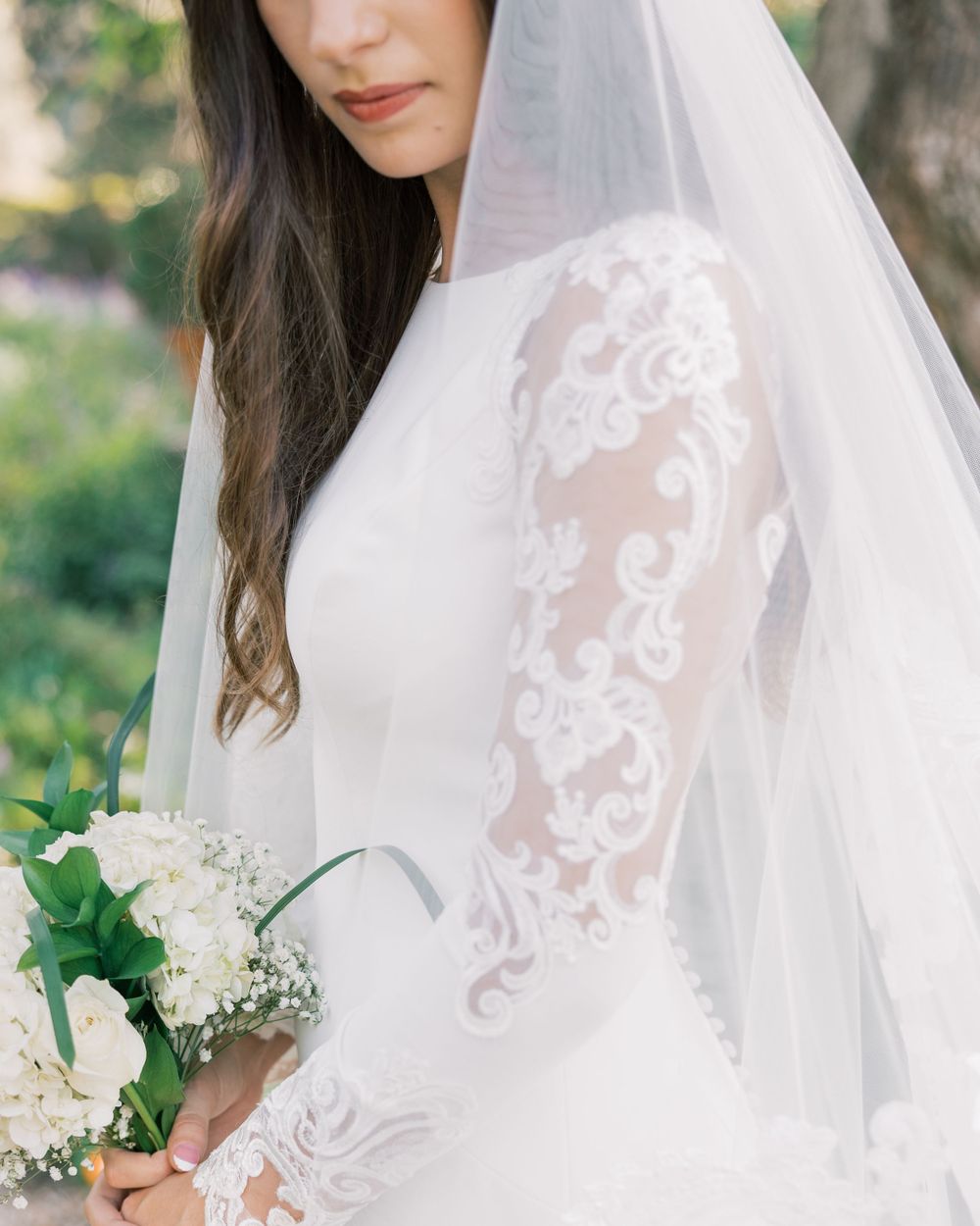 Close-up detail of lace sleeve and white bouquet against wedding dress.