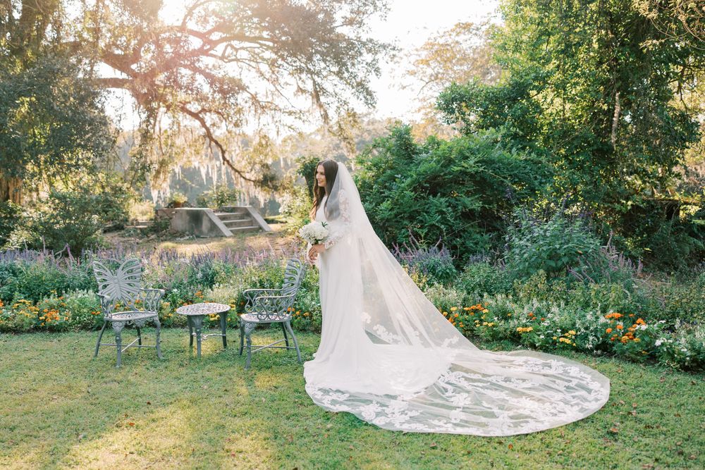 Wedding dress with cathedral train displayed in garden with vintage chairs.
