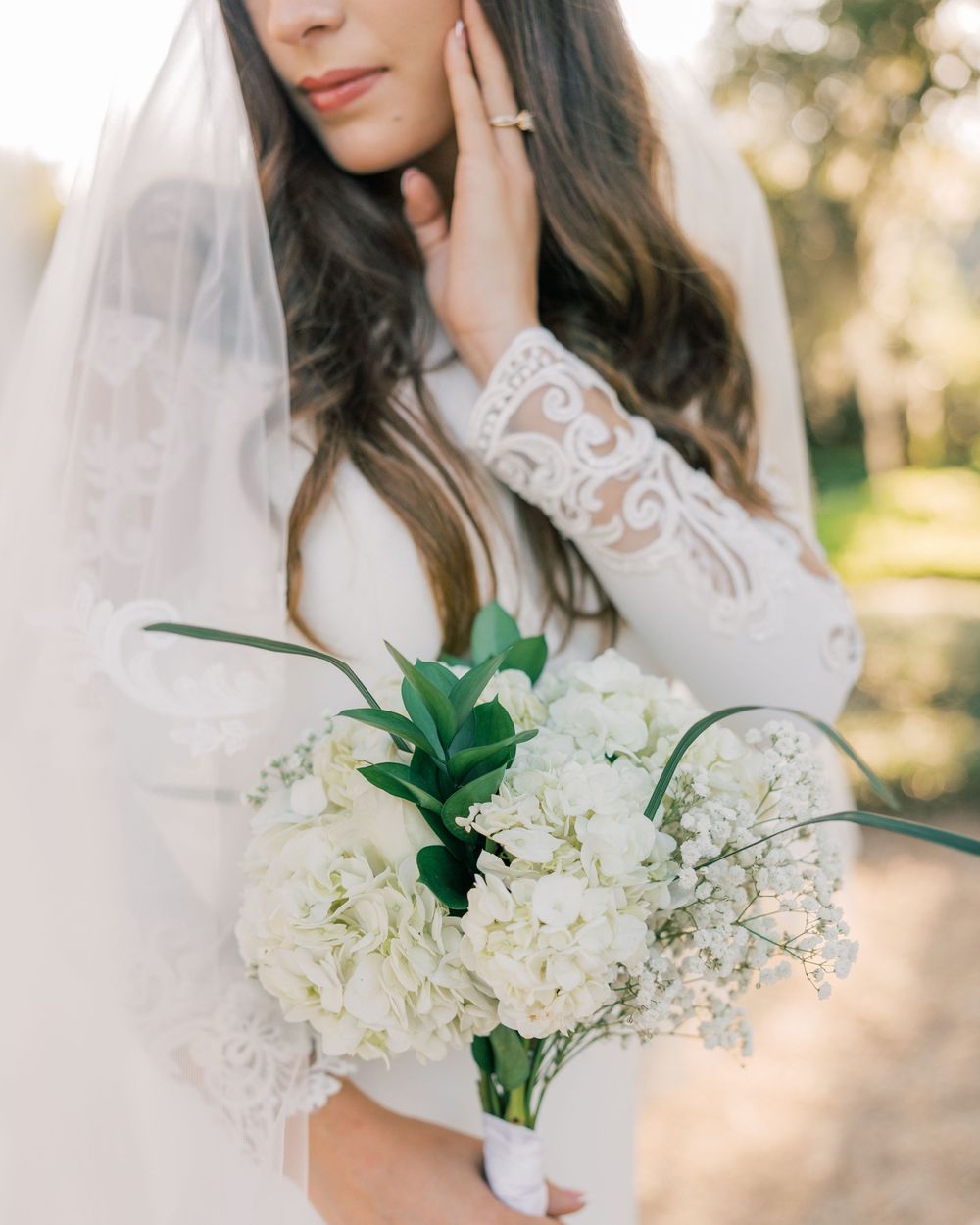 Artistic detail shot of white hydrangea bouquet with lace sleeve and veil.