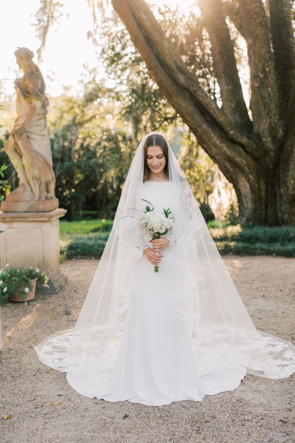 Classic bridal portrait featuring a long-sleeved white gown and dramatic cathedral veil in a garden.