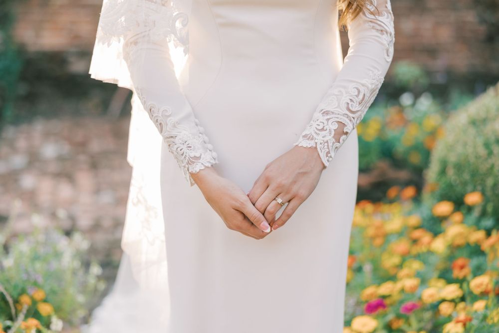 Close-up detail of lace sleeves and wedding ring against a garden background.
