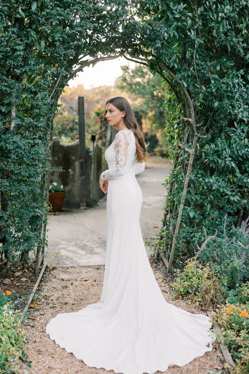Ethereal bridal portrait under a garden archway with trailing lace gown and veil.