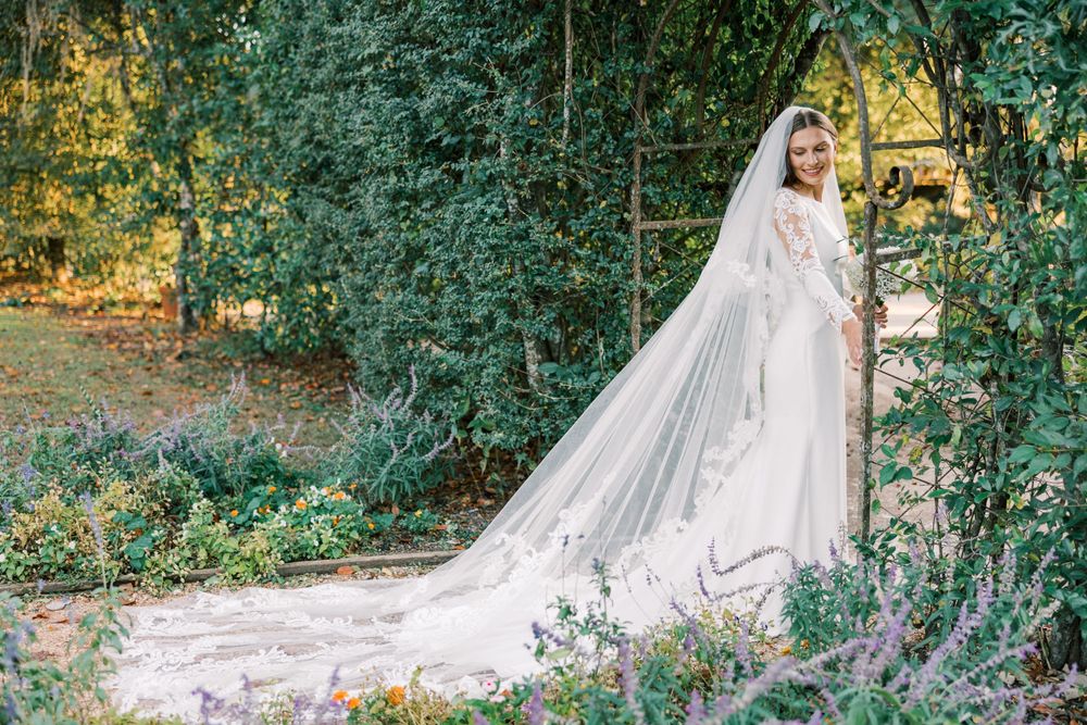 Romantic garden wedding photo with flowing cathedral veil and lush greenery backdrop.