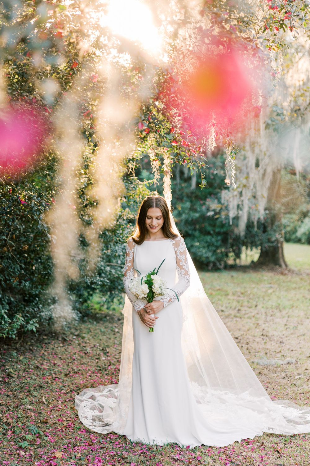 Ethereal bridal photo with soft sunlight filtering through trees and pink floral elements.
