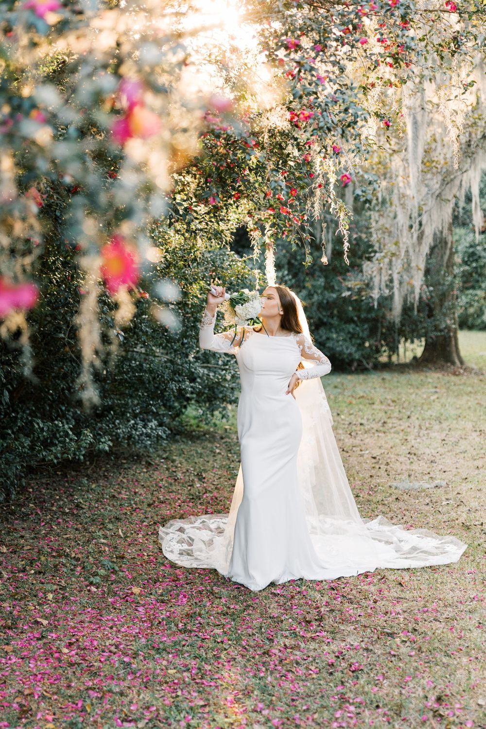 Joyful bridal moment captured in a garden setting with falling pink petals and golden sunlight.