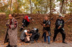 LARP participants in medieval costumes pose with prop weapons in autumn forest setting.
