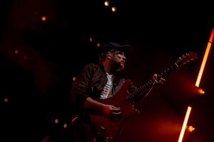 Musician performs with red electric guitar under dramatic red stage lighting.
