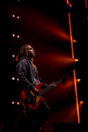 Bass guitarist performs on stage with red instrument under dramatic orange lighting effects.