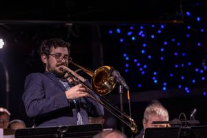 A trombone player performs on stage with blue lights glowing in the background.