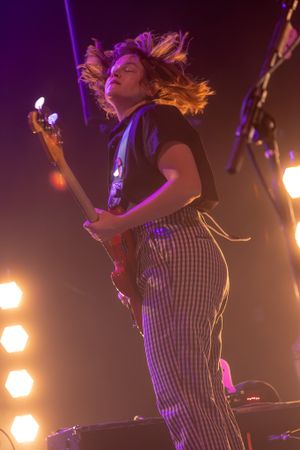 Guitarist performs energetically with flowing hair under purple stage lights.