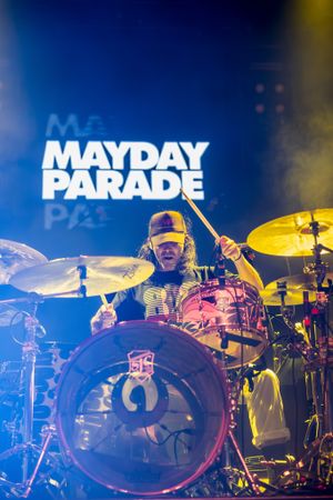Drummer performs behind drum kit with Mayday Parade logo illuminated in blue lighting.
