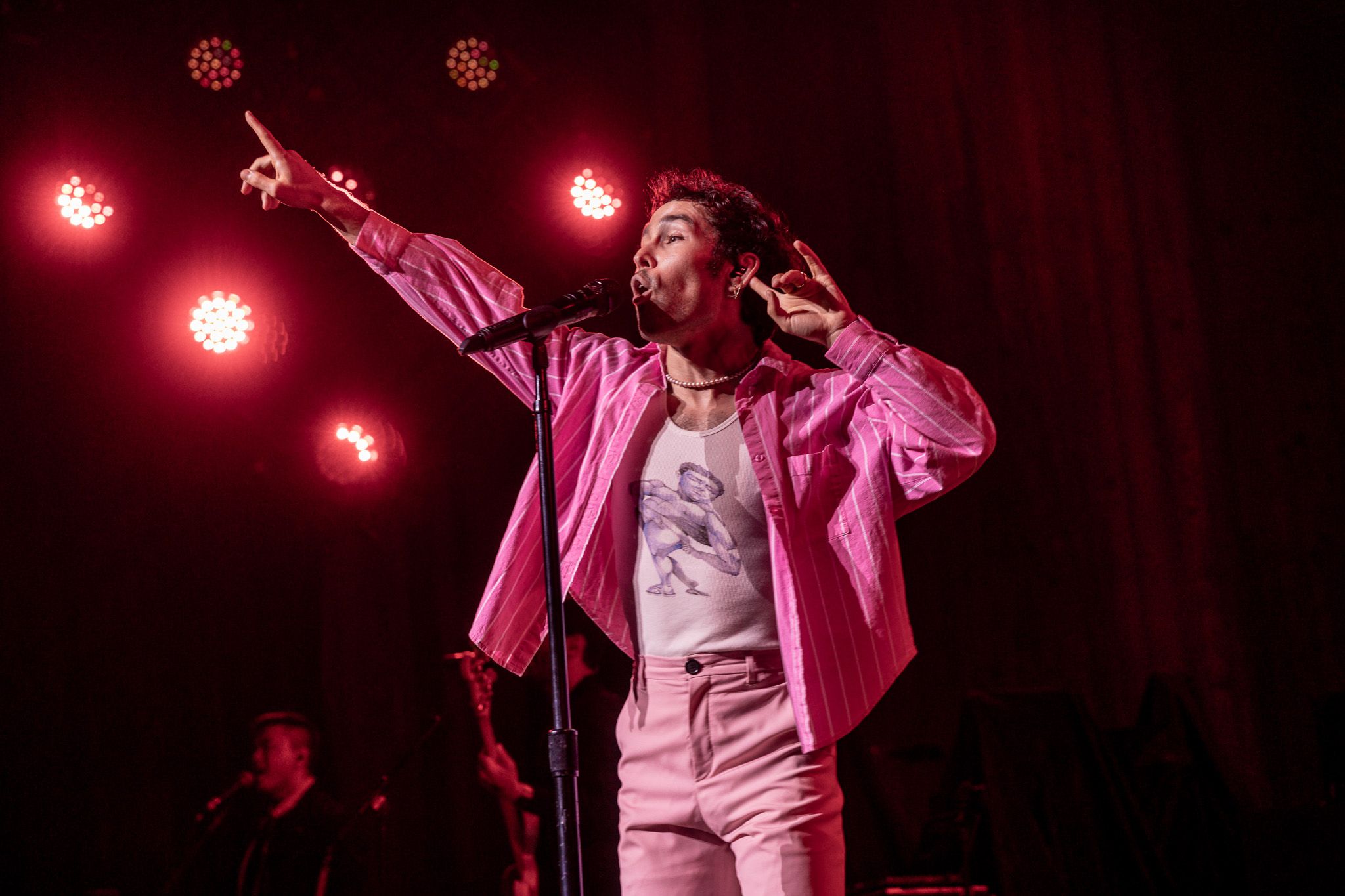 Stage performer in pink outfit energetically singing under red spotlights.