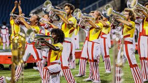 Brass band members in red and white striped uniforms play their instruments in formation.