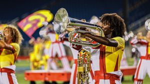 Brass players in yellow and white uniforms perform on stage with dramatic lighting.