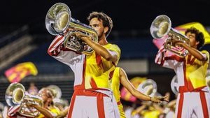 Trumpet players in yellow and red uniforms perform during a nighttime marching show.